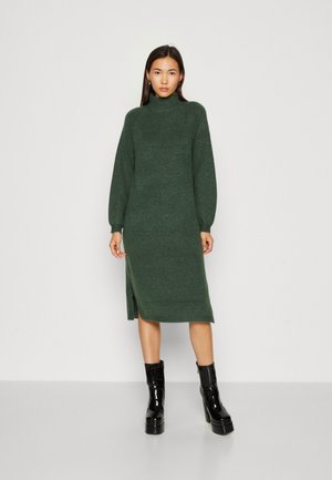 Strikket grøn turtleneck kjole med lange ballonærmer, sideslids og afslappet pasform. Sæt den sammen med glinsende sorte platform ankelstøvler.