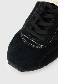 Mustmustad sneakerite polo musta nööridega ja valge topeltõmblusega valgel taustal.