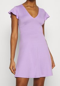 Lila kort klänning med djup V-ringning, korta ärmar, åtsittande kropp och utställd kjol. Tillverkad av mjukt, stretchigt material.