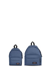 Dvě modré batohy jsou vystaveny, jeden větší než druhý. Oba mají kulatý tvar, přední kapsu, zipy a horní držadlo.