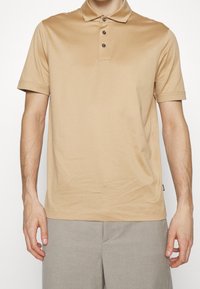 Beige polotröja i ett mjukt tyg, med krage, treknappling och korta ärmar. Inga synliga mönster eller detaljer.