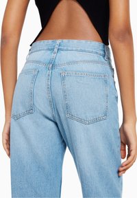 Vista trasera de una persona que lleva jeans de tiro alto de color azul claro y una blusa sin mangas negra que revela la parte baja de la espalda.