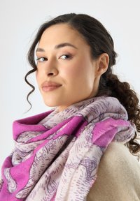 Sciarpa a motivi rosa e beige realizzata in tessuto morbido, con un design dettagliato e bordi sfilacciati, avvolta attorno al collo.