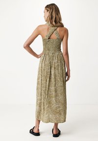 Maxiklänning i olivgrön med smockad byst, korskorsade axelband och ett bladmönster. Tyget verkar lätt och har en flödande siluett.