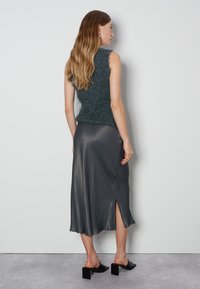 Ärmelloses türkisfarbenes Stricktop aus strukturiertem Stoff, kombiniert mit einem dunkelgrauen Satinrock mit Schlitz und schwarzen Blockabsatzsandalen.