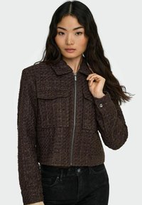 Pruun tekstuuriga lühike jakk luku eesosaga, kahe rinnatasku ja kraega kaelusega. Kangas on kootud mustriga ja pehme viimistlusega.