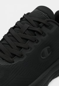 Μαύρο αθλητικό παπούτσι με υφασμένη επιφάνεια, τυπικά κορδόνια και εμφανές λογότυπο της μάρκας. Διαθέτει ενισχυμένη σόλα και ομαλές λεπτομέρειες.