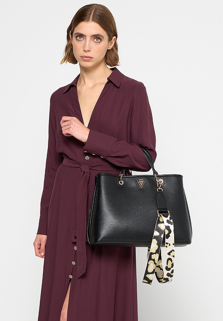 Borsa a tracolla in pelle nera con finiture dorate e una tracolla rimovibile, caratterizzata da un motivo a stampa leopardata, portata da una persona in un vestito viola.
