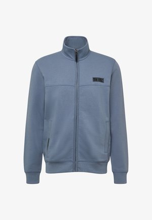 Veste en polaire bleu zippée avec un col haut, deux poches latérales et une patch logo noire sur la poitrine. Texture lisse et poignets élastiques.