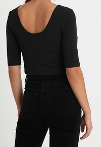 Sort cropped top med en bred scoop-ryg, tætsiddende design og ærmer, der går til albuen; stoffet fremstår glat og strækbart.