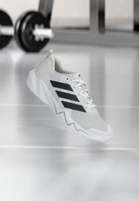 White athletic shoe with a textured mesh upper, featuring three black stripes, a ridged sole, and light blue accents.