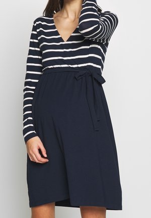 Pasiasta sukienka z długim rękawem w kolorze granatowym i białym, z dekoltem w kształcie litery V, wiązaniem w talii i rozkloszowanym dołem. Wykonana z miękkiego, rozciągliwego materiału.