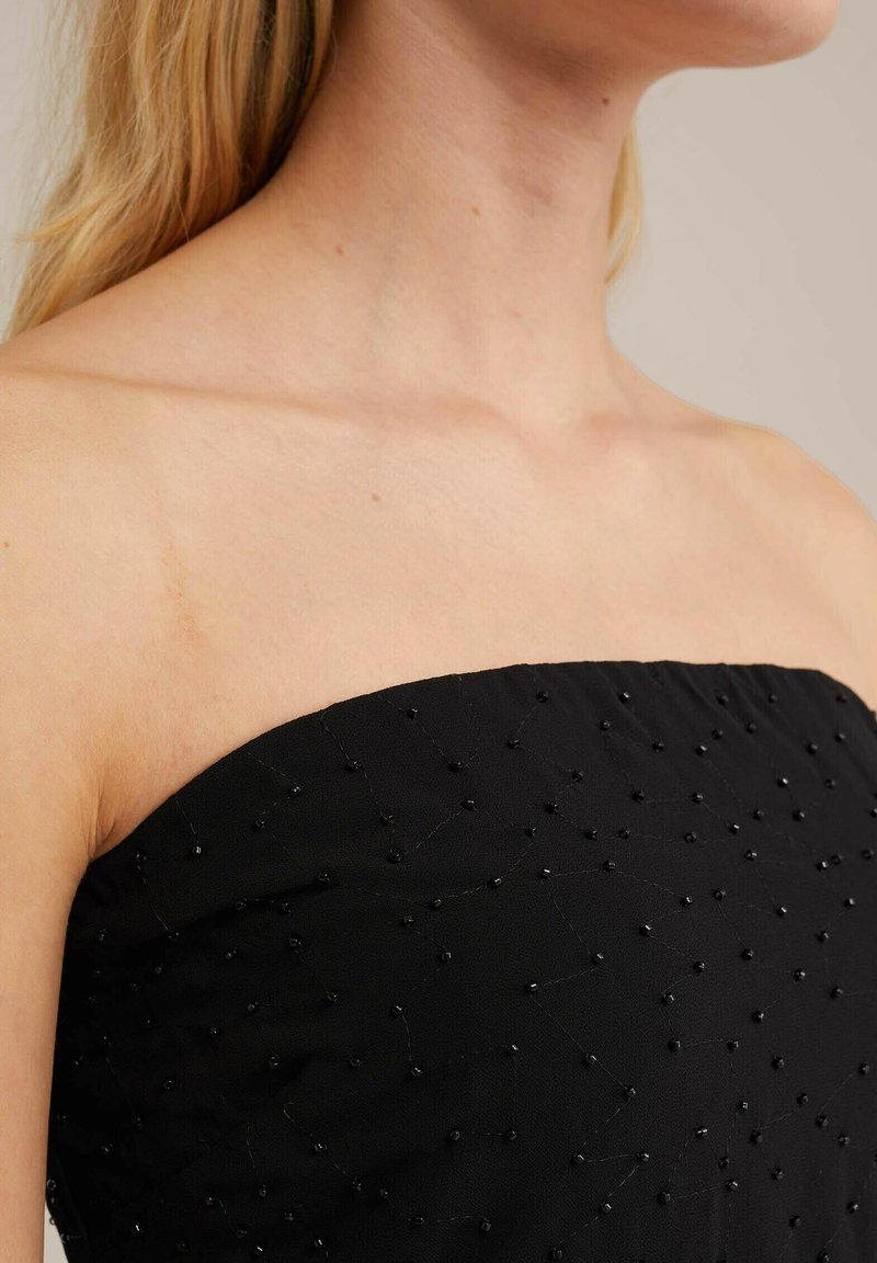 Top negro sin mangas con detalles de cuentas, tela texturizada y una silueta estructurada. La notable ornamentación con cuentas crea un patrón sutil en la superficie.