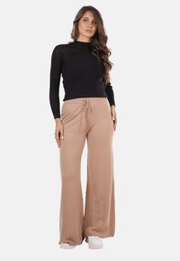 Top lungo a maniche lunghe nero a coste abbinato a pantaloni beige larghi con vita regolabile. Modella che indossa sneakers bianche.