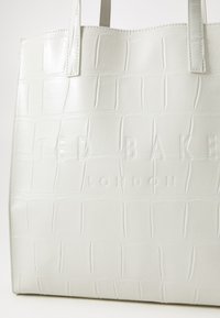 White crocodile-embossed leather tote bag with dual handles. Features debossed "TED BAKER LONDON" logo on the front. Smooth texture.