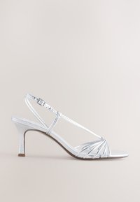 Ezüst színű, vékony pántos, magas sarkú szandál texturált felülettel, vékony bokapántokkal és kúpos sarokkal, keresztpántos kialakítással a lábujjnál.