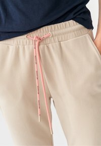 Beiga sweatpants med en ribbad midja och en rosa dragsko. Slät yta med logotypdetaljer på dragskon.