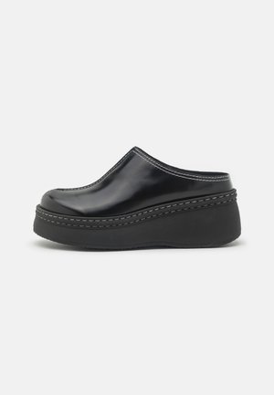 Black glossy platform clogs with a rounded toe, curved upper, and contrasting white stitching along the edge of the sole.