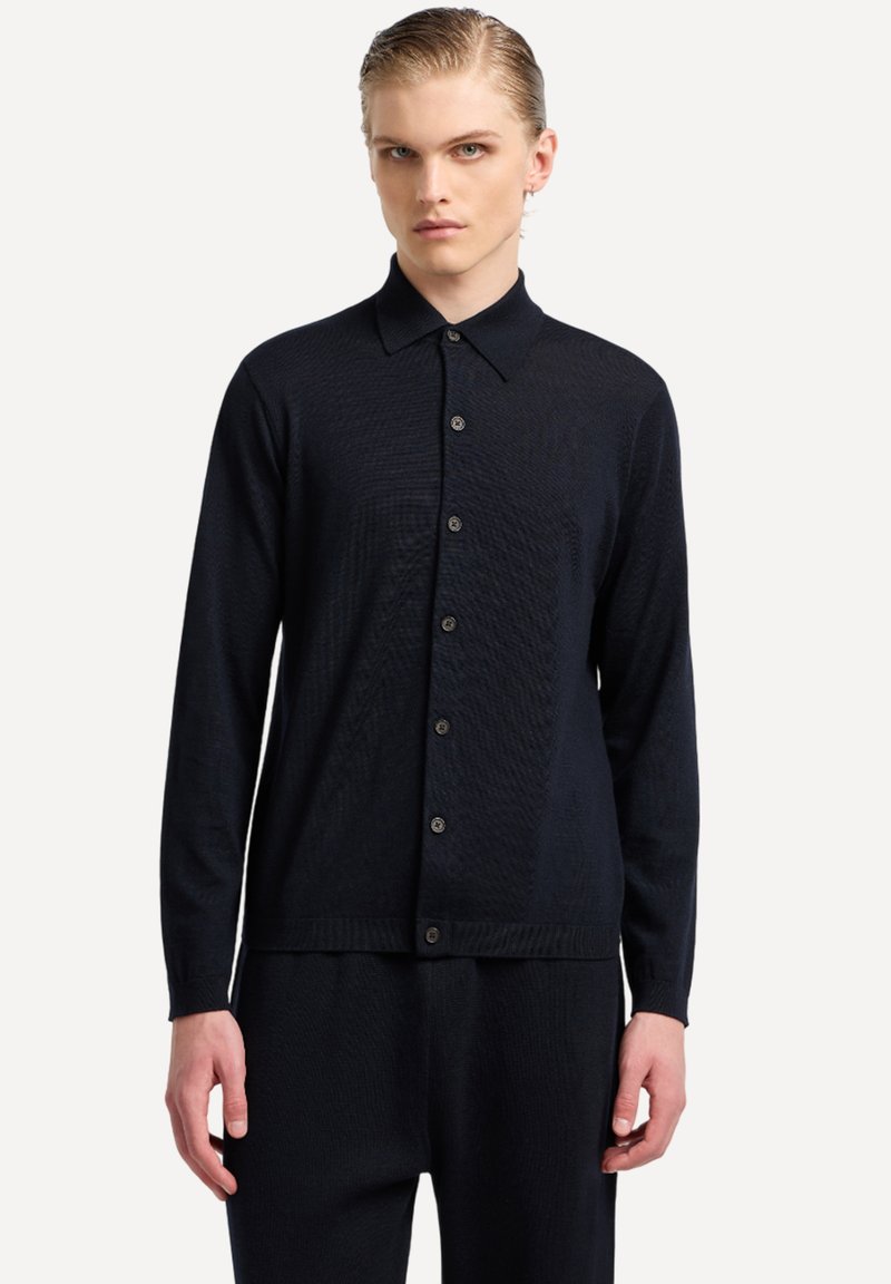 Camicia blu navy a maniche lunghe con bottoni. Tessuto leggero e strutturato, con colletto classico e cinque bottoni sul davanti. Design aderente.