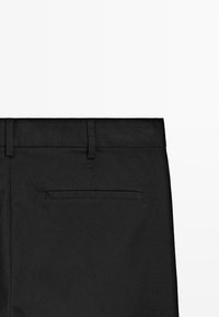 Černé kalhoty s plochým předním dílem, poutky na pásek a jednou zadní kapesní lištou. Tkanina má hladký, texturovaný vzhled.