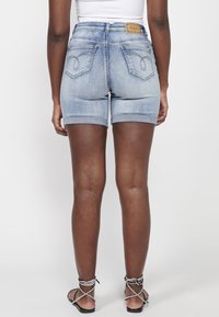 Shorts en jean bleu clair avec une taille haute, ourlets retroussés, couture décorative sur la poche arrière et un patch en cuir beige au dos.