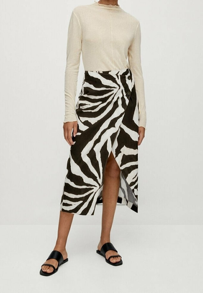 Personne portant un haut beige à manches longues et une jupe portefeuille à motif zèbre noir et blanc avec des sandales noires.