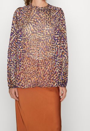 Mujer con una blusa de manga larga y transparente con patrones abstractos en púrpura, naranja y beige, y una falda color óxido.