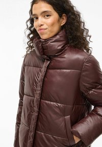 Bordo puf jakna s visokim ovratnikom, s sjajnom završnom obradom, horizontalnim kvadratom i bočnim džepovima.