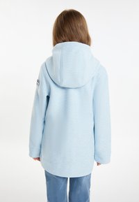 Ljusblå fleece-hoodie med en texturerad yta, långa ärmar och en något längre bakhem. Har en logotyp på ärmen.