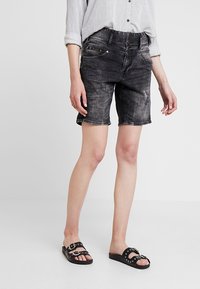 Svarta denimshorts med blekt mönster, midjehöjd och fem fickor. Matchas med en randig långärmad skjorta och svarta sandaler.