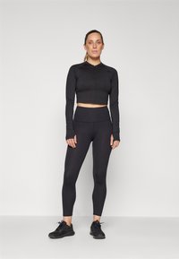 Čierny atletický set pozostávajúci z crop topu s dlhým rukávom a predným zipsom a legín s vysokým pásom vyrobených z hladkej, elastickej látky.