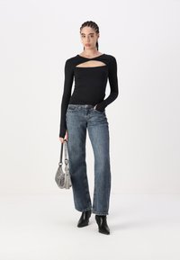 Black long-sleeve top with a cut-out design, paired with wide-leg blue denim jeans. Accessorized with a small silver handbag and black heels.