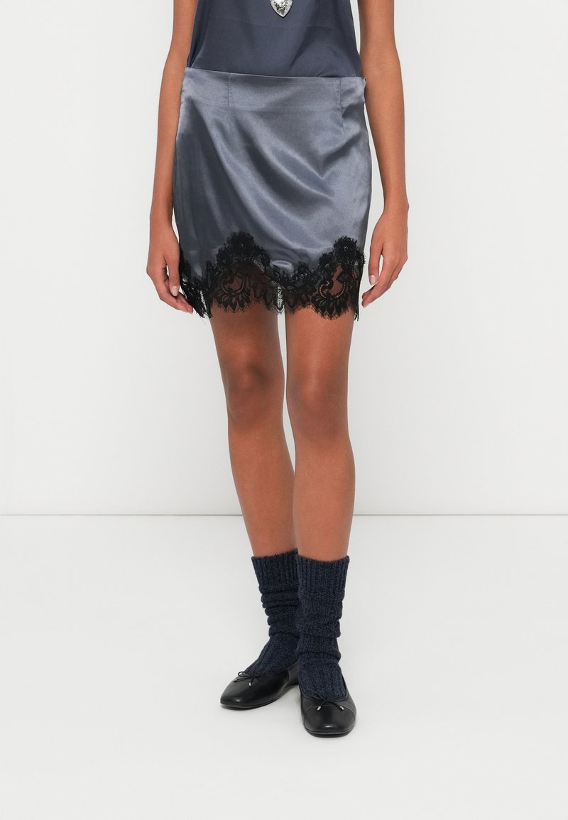 Szürke szatén miniszoknya fekete csipkeszegéllyel, hozzá párosítva tengerészkék kötött zokni és fekete balettcipő. Sima textúra csipkedíszítéssel.