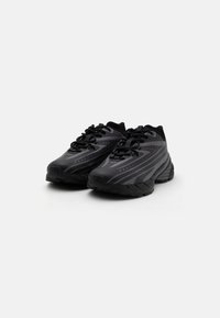 Des chaussures de sport noires avec un design élégant, un dessus texturé, un laçage et une semelle en caoutchouc épaisse avec des accents rayés saisissants.