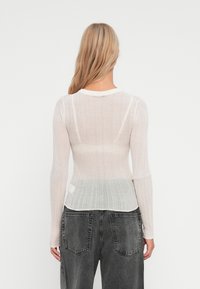 Top a maniche lunghe in maglina a coste, con sfumatura dal bianco al grigio chiaro, caratterizzato da un collo rotondo e un design aderente. Vista posteriore che mostra la texture e il motivo.