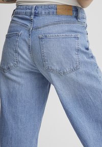 Svetlo modri denim jeans s sproščenim krojem, ki vključujejo zadnje žepe in usnjeno označbo z napisom "PULZ JEANS" na pasu.