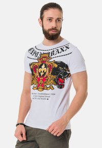 Weißes T-Shirt mit kurzen Ärmeln, das mit einem auffälligen Grafikdesign eines Panthers, einer Krone und verschnörkelten Mustern in roten, goldenen und schwarzen Akzenten verziert ist.