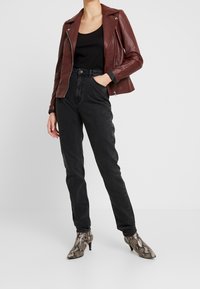 Chaqueta de motorista de cuero burdeos sobre una blusa negra, combinada con jeans negros de tiro alto y botines de tacón con estampado de serpiente.