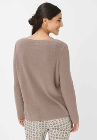 Pull en tricot côtelé de couleur brun clair avec un col large, des manches longues et une coupe décontractée, associé à un pantalon ajusté à motifs.