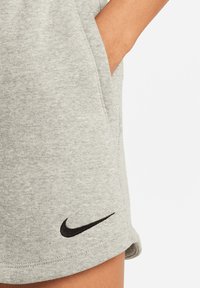 Grijze, zachte stoffen shorts met zijzakken en een zwart Nike-logo geborduurd dichtbij de zoom. De zoom is lichtjes gebogen.