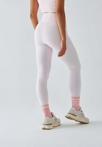 Białe legginsy z wysokim stanem, ozdobione różowymi akcentami. W połączeniu z beżowymi trampkami i różowymi skarpetkami w paski z napisem.