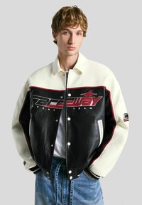 Veste bomber en cuir noir avec des manches crème, des accents rouges et le logo "Raceway Sport Team". Dotée de boutons pression et de poignets côtelés.