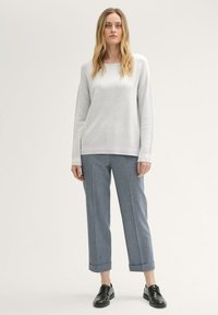 Lichtgrijze trui met een visgraatpatroon, gecombineerd met lichtblauwe wijde broek. Model draagt zwarte veterschoenen en staat tegen een neutrale achtergrond.