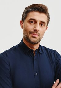 Granatowa koszula zapinana na guziki z kołnierzykiem, gładka tkanina z lekkim połyskiem i długimi rękawami, noszona przez mężczyznę z złożonymi rękami.