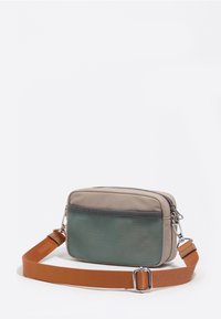 Kompaktowa prostokątna beżowa torebka na ramię z przednią szarą siateczkową kieszenią i regulowanym szerokim pomarańczowym paskiem z metalowymi zapięciami.