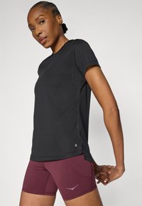 Μαύρο αθλητικό κοντομάνικο με υφή υφάσματος, σε συνδυασμό με μπορντό εφαρμοστά σορτς με διακριτικό λογότυπο στο πλάι.