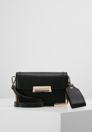 Black leather crossbody bag with gold hardware, front clasp, detachable strap, and an attached wide leather tag on a white surface.