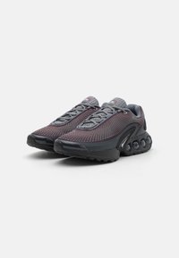 Un paio di scarpe da ginnastica grigio scuro con upper in tessuto a motivi, suole nere rotonde dotate di cuscinetti d'aria circolari e lacci grigi.