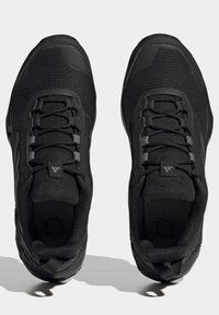 Baskets de sport noires avec une tige en mesh texturé, fermeture à lacets, talon moulé et semelle extérieure en caoutchouc pour plus de traction. Présente des accents de marque minimaux.