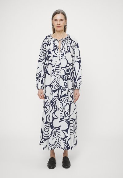 Pitkä mekko tummansinisenä ja valkoisena abstrakteilla kuvioilla. Siinä on pitkät hihat ja ry gathered kaula-aukko. Yhdistetty mustiin liukuviin kenkiin.